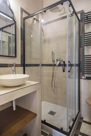 A modern bathroom with a glass-enclosed shower, a white sink, and a mirror. - Cozy Family Stay at the Colosseum (Roma)