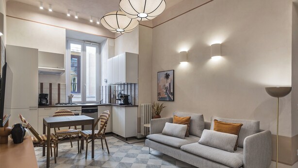 Ein modernes Wohnzimmer mit Sofa, Esstisch und Stühlen, im Hintergrund eine Küche und ein großes Fenster.