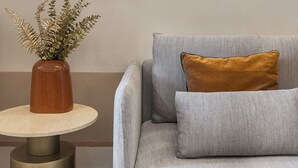 Ein Zimmer mit einem grauen Sofa, einem runden Tisch mit einer braunen Vase und einem Gemälde von einer Palme und Architektur.