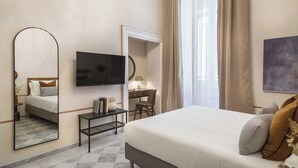 Ein Hotelzimmer mit Bett, Schreibtisch, Stuhl, Fernseher, Spiegel und einem fensterbepflanzten Fenster.