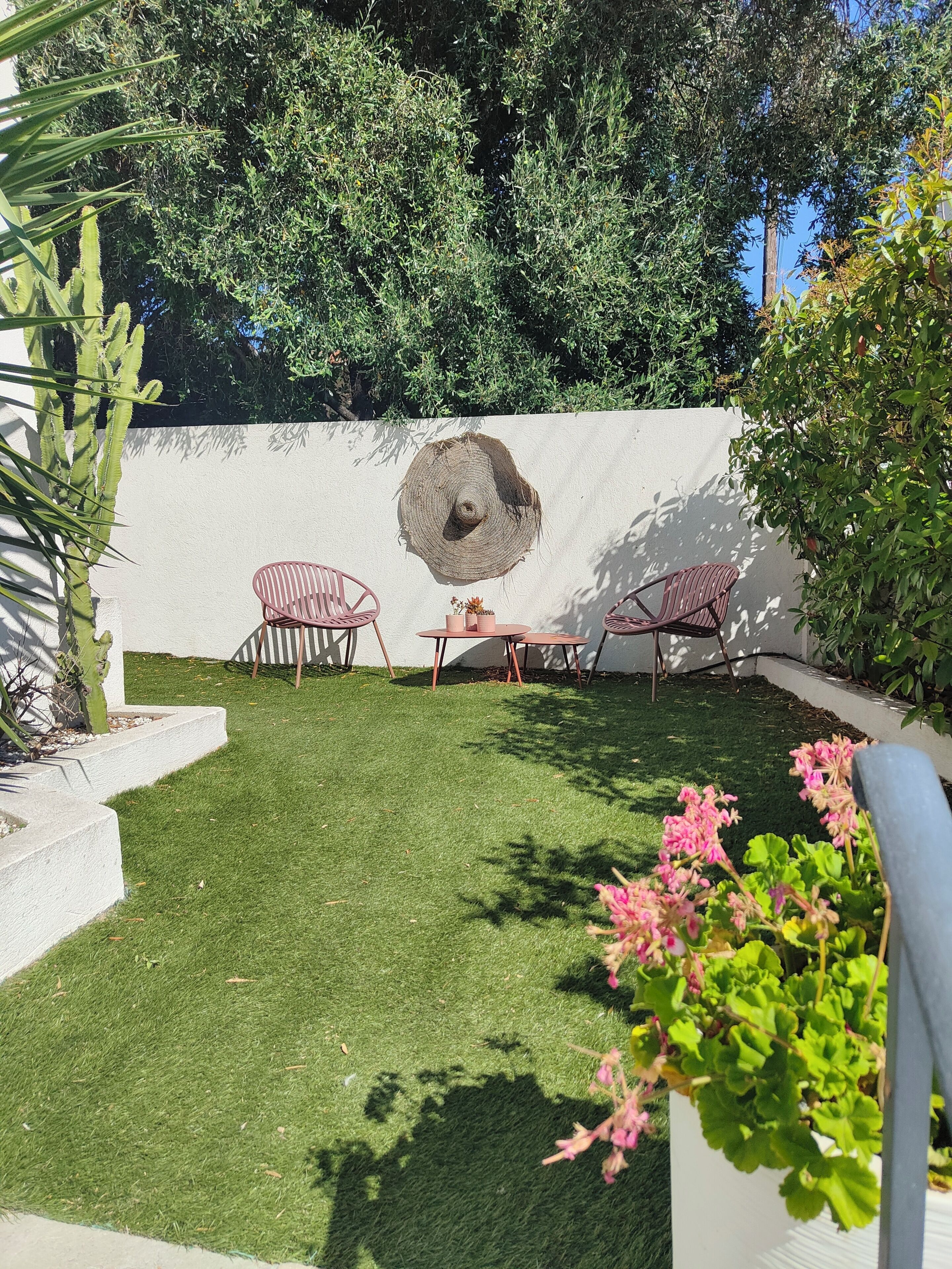 A patio with artificial grass, two chairs, a table, and a large tree trunk decoration.