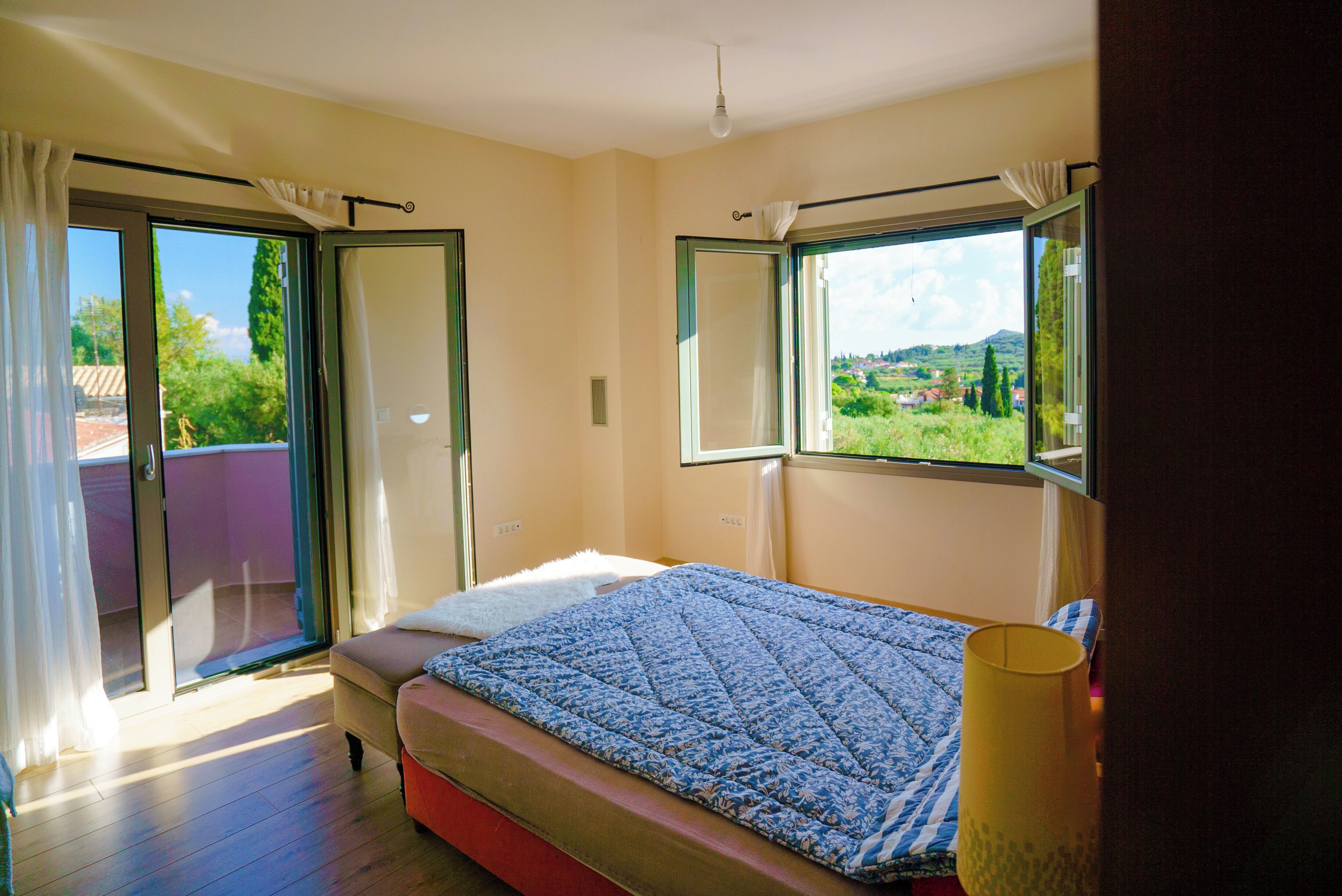 A bedroom with a bed, a window with a view, a sliding glass door, and a ceiling light.