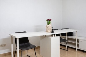 Un espacio de oficina minimalista con una mesa blanca, sillas negras y un jarrón decorativo con flores rojas.