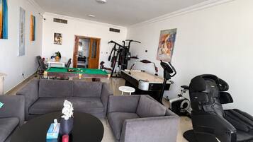 A living room with a pool table, sofas, a massage chair, and exercise equipment.