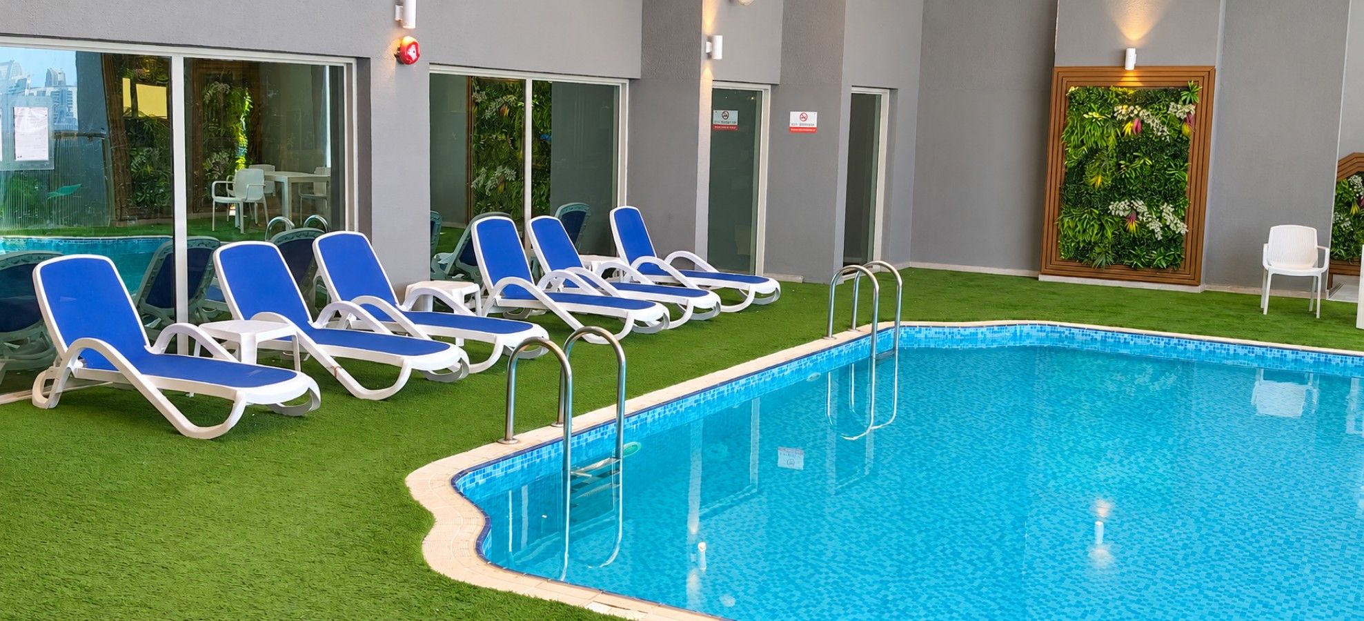 A swimming pool with blue water, surrounded by white and blue lounge chairs, and a green artificial grass area.