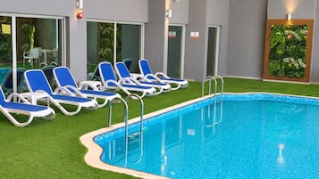 A swimming pool with blue water, surrounded by white and blue lounge chairs, and a green artificial grass area.