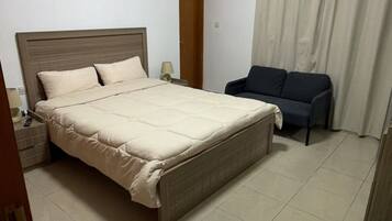 A hotel room with a bed, a sofa, a nightstand, a lamp, and a picture on the wall.