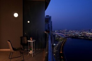 Un balcon offrant une vue sur le paysage urbain au crépuscule, avec une chaise, une petite table et une plante en pot.