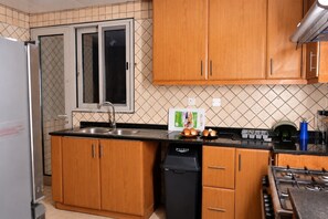 A compact kitchen with wooden cabinets, a stainless steel sink, a dishwasher, and a gas stove. - Private King Room | Side Lake View | Sharjah (Sharjah)