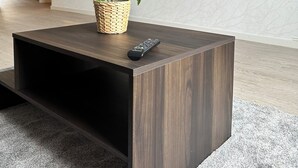 Ein modernes Wohnzimmer mit einem dunkelholzigen Couchtisch, einem Blumentopf, einer Fernbedienung, einem Flachbildfernseher und einem gewebten Korb.