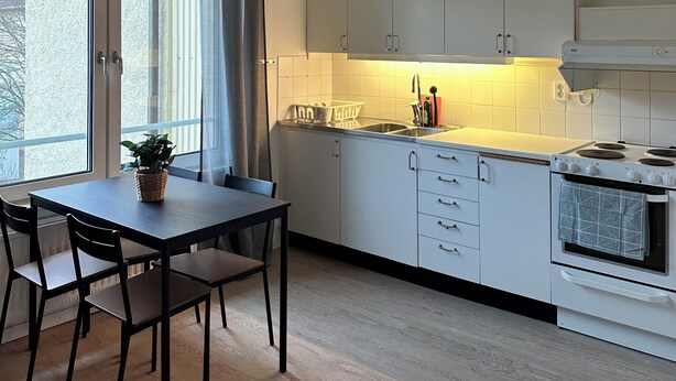 Eine moderne Küche mit weißen Schränken, einem Esstisch mit Stühlen und einem großen Fenster mit Vorhängen.