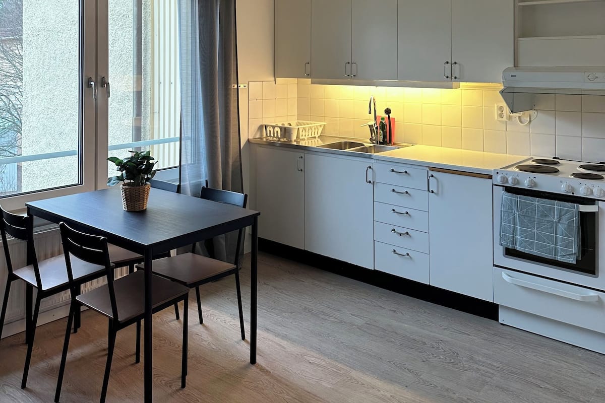 A modern kitchen with white cabinets, a dining table with chairs, and a large window with curtains.