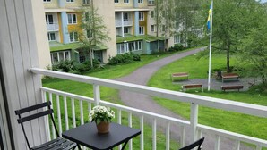 Ein Balkon mit Tisch und Stühlen, der auf eine grüne Rasenfläche und ein Gebäude mit vielen Fenstern blickt.