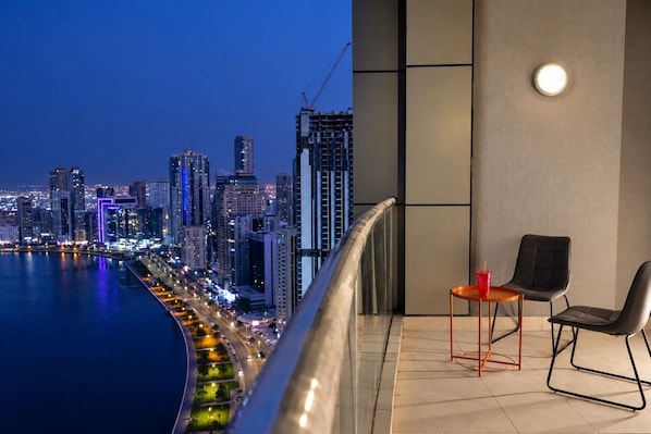 En balkon med udsigt over byens skyline i skumringen, med moderne bygninger og en havnefront.