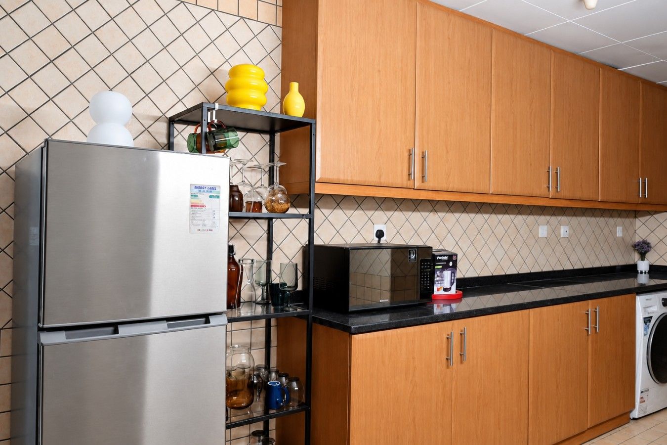 Eine Küche mit einem Edelstahl-Kühlschrank, einer Mikrowelle, Holzschränken und einer schwarzen Arbeitsplatte.