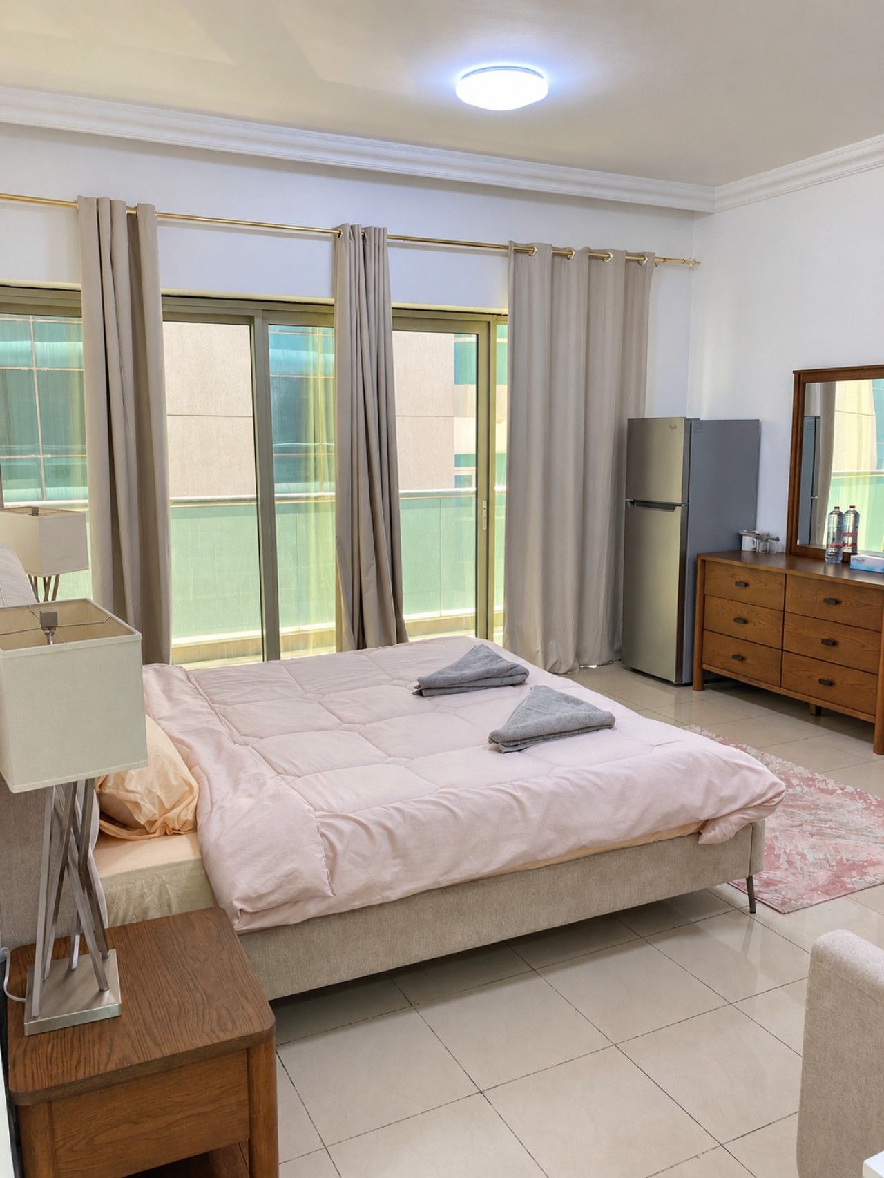 A hotel room with a bed, a dresser, a mirror, a lamp, and a window with curtains.