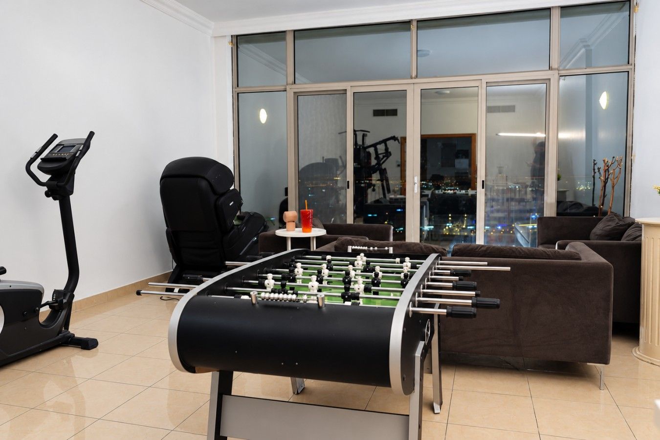 A room with a foosball table, a treadmill, and a large window with a city view.