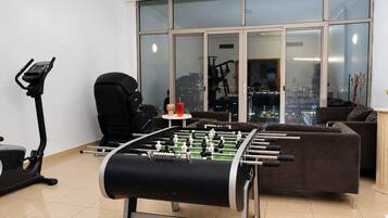 A room with a foosball table, a treadmill, and a large window with a city view.