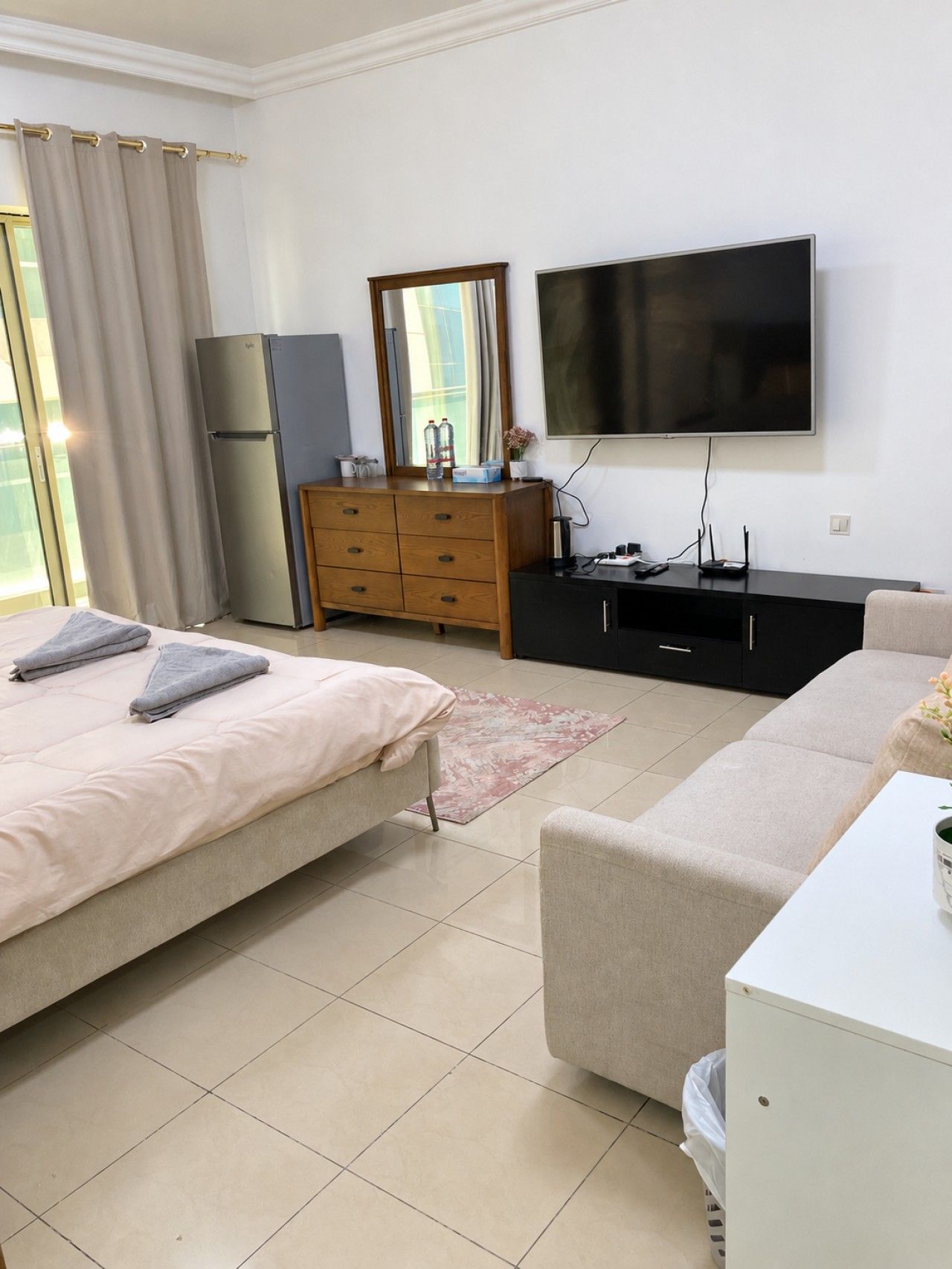 A bedroom with a bed, a dresser, a television, and a window with curtains.