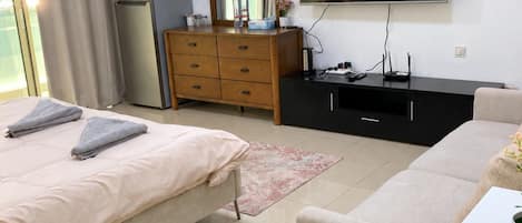 A bedroom with a bed, a dresser, a television, and a window with curtains.