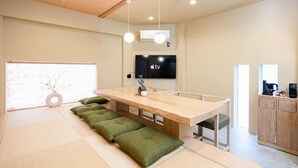 Un interior moderno con una mesa de comedor de madera, cojines verdes, un televisor de pantalla plana y una zona de cocina.