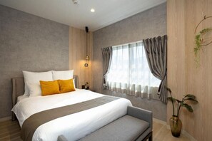 Une chambre moderne avec un grand lit, un banc, une table de chevet, une lampe fixée au mur et une fenêtre avec des rideaux.