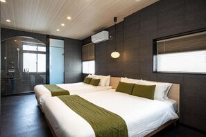 Une chambre d’hôtel moderne avec deux lits, une douche en verre et une grande fenêtre avec stores.