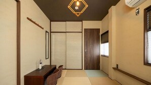 Una habitación tradicional japonesa con suelo de tatami, una mesa de madera baja con sillas, una puerta corredera y una lámpara en el techo.