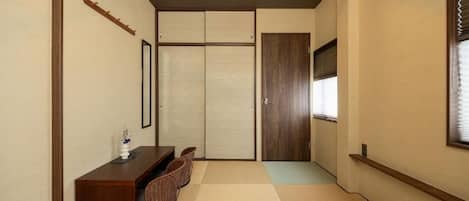 Una habitación tradicional japonesa con suelo de tatami, una mesa de madera baja con sillas, una puerta corredera y una lámpara en el techo.