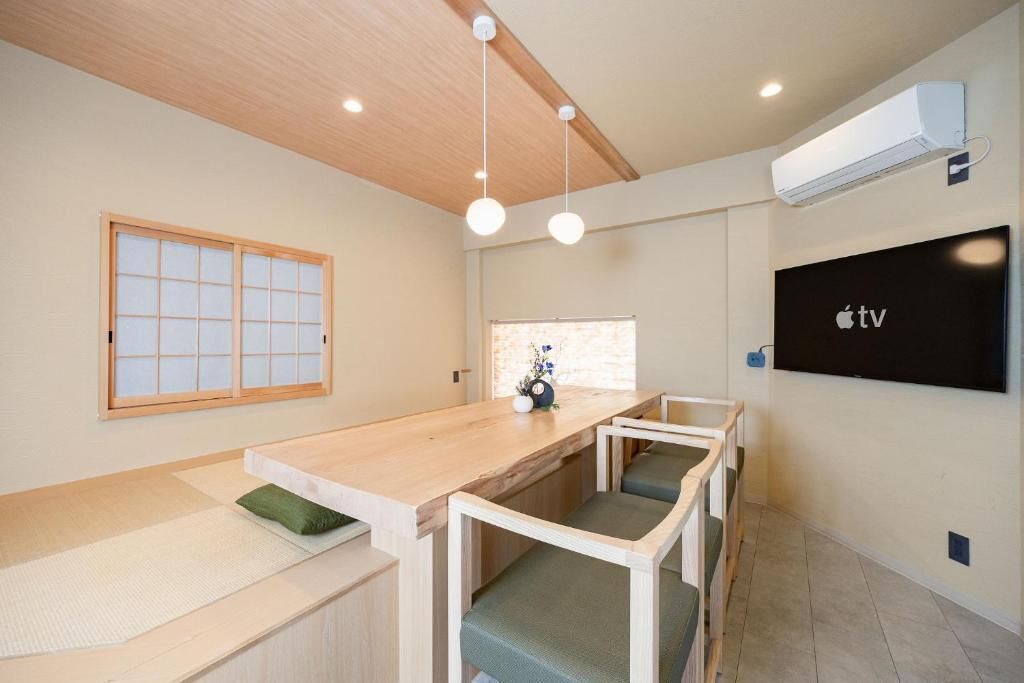 A room with a wooden table, chairs, a TV, and a window with a grid pattern.