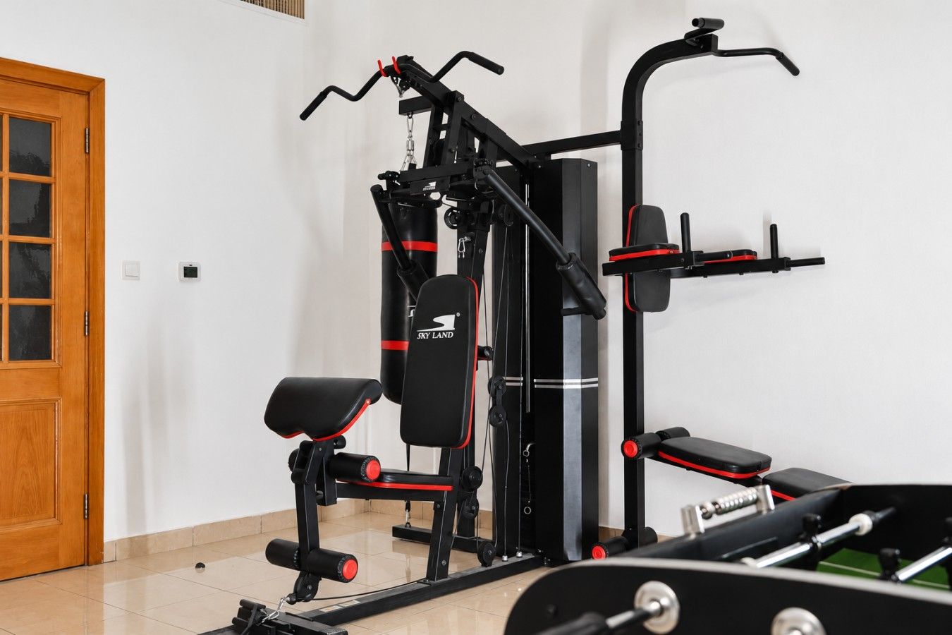 A home gym with exercise equipment including a bench press, a pull-up bar, and a cable machine.