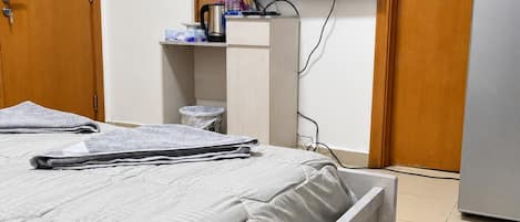 A hotel room with a bed, a television mounted on the wall, a small wooden desk, and a refrigerator.