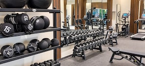 Et fitnessrum med forskellig træningsudstyr, herunder håndvægte, medicinbolde og løbebånd.