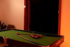 A pool table with balls and cues, a chair, and a window.