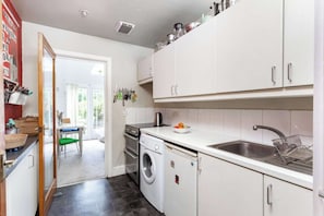 A compact kitchen with white cabinets, a washing machine, a sink, and a dining area visible through an open door. - Charming 1BDR Flat in Stockwell (Greater London)