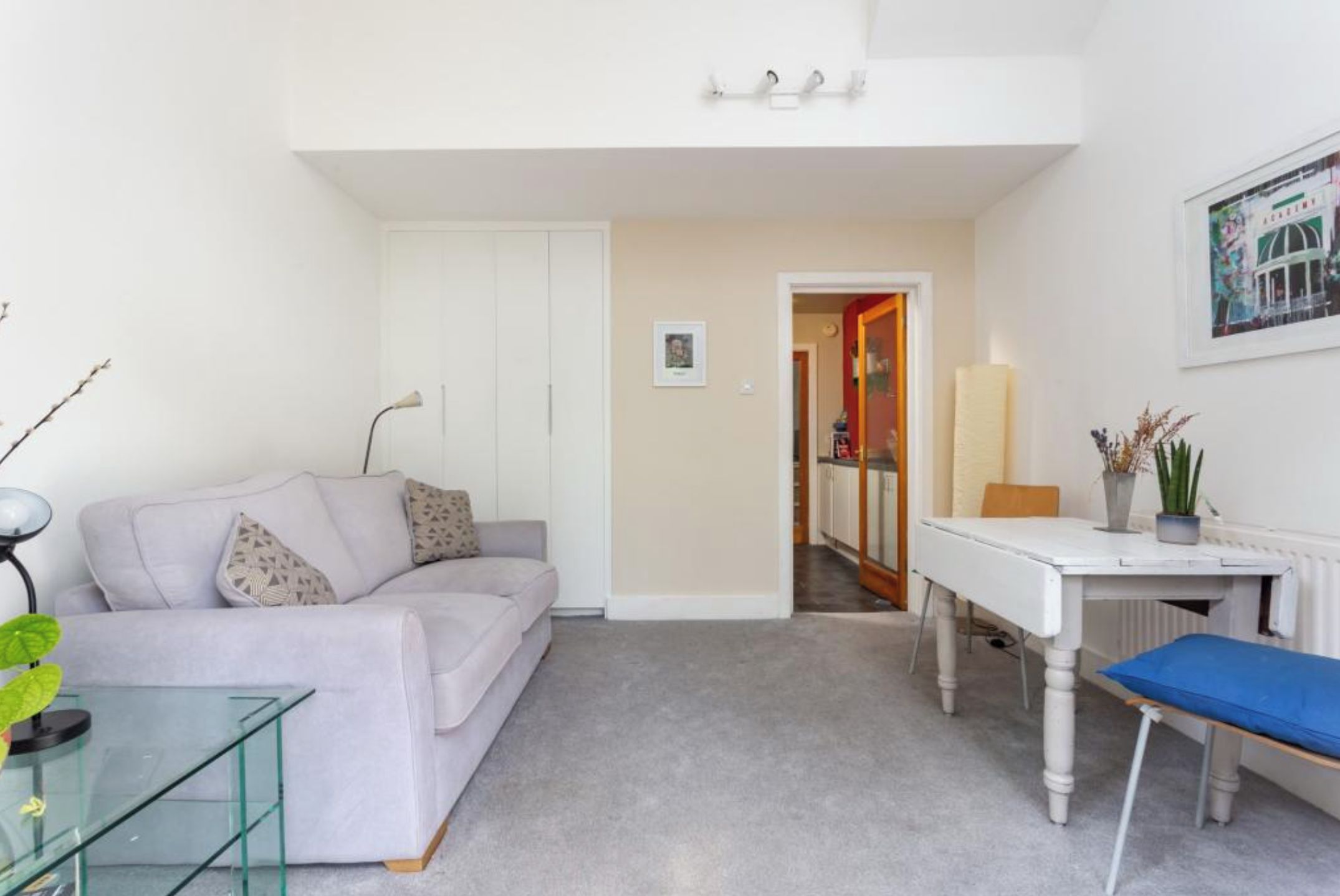 A compact living space with a sofa, a glass coffee table, a desk with a chair, and a radiator.