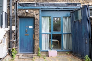 A blue door with a number plate, a window with curtains, and a small stool outside. - Bright 1BDR Flat in the heart of Little Portugal (Greater London)