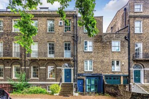 A row of brick townhouses with multiple windows, a blue door, and a small garden area. - Charming 1BDR Flat in Stockwell (Greater London)