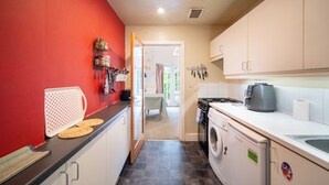 Eine kleine Küche mit roter Wand, einer Waschmaschine und einer Kaffeemaschine.