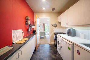 A compact kitchen with a red wall, a washing machine, and a coffee maker. - Bright 1BDR Flat in the heart of Little Portugal (Greater London)