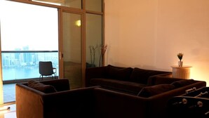 Un salon moderne avec un canapé, un fauteuil et une vue sur le paysage urbain, visible à travers une porte vitrée.