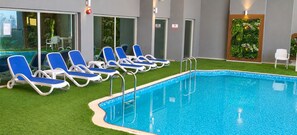 A swimming pool with blue water, surrounded by white and blue lounge chairs, and a green artificial grass area.
