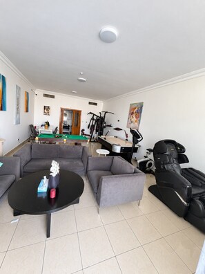 Una sala de estar con mesa de billar, sofás, sillón de masaje y equipo de ejercicio.