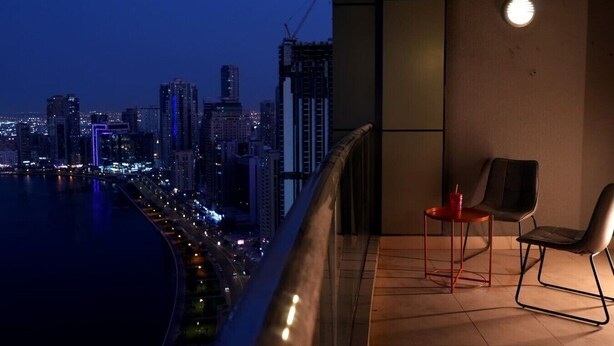 Un balcon offrant une vue sur le paysage urbain au crépuscule, avec des bâtiments modernes et un front de mer.