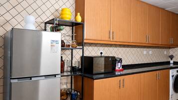 A kitchen with a stainless steel refrigerator, a microwave, wooden cabinets, and a black countertop.