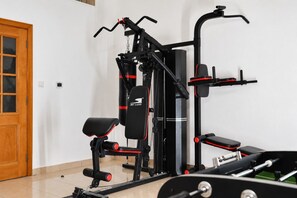 Een sportschool thuis met trainingsapparatuur, waaronder een bankdrukapparaat, een optrekstang en een kabeltrekapparaat.