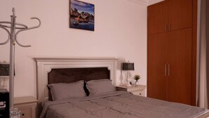 Une chambre à coucher comprenant un lit, une table de chevet, une lampe, un tableau représentant un paysage urbain et une armoire.