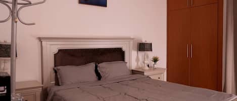 A bedroom with a bed, a nightstand, a lamp, a picture of a cityscape, and a wardrobe.