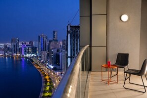 Un balcón con vistas a un horizonte urbano al atardecer, con edificios modernos y una zona costera.