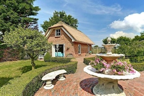 A brick house with a thatched roof, a garden with a fountain, and a bench. - Holiday home in Den Helder with barbecue (Den Helder)